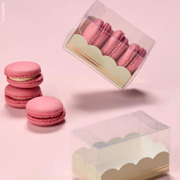 Scatoletta trasparente porta macarons, una vuota ed una con dei macarons rosa e tre macarons rosa sul tavolino fuori dalle scatole